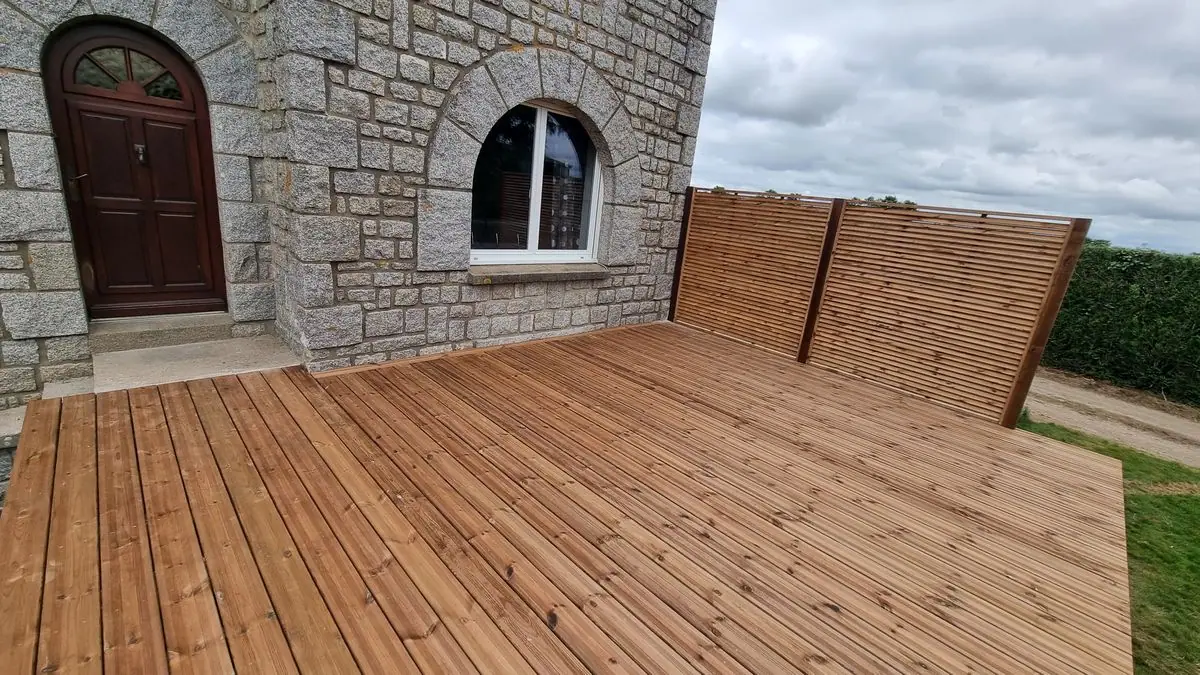 Une terrasse en bois et ses claustras au pied d’une maison en pierre